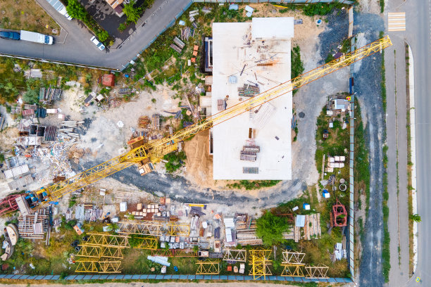 从直升机上鸟瞰城市之间未完工的建筑，工业设备，起重机，底部移动的小车图片下载