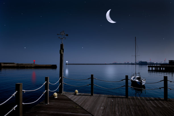 新月升起在帆船风向标和灯塔上。图片下载