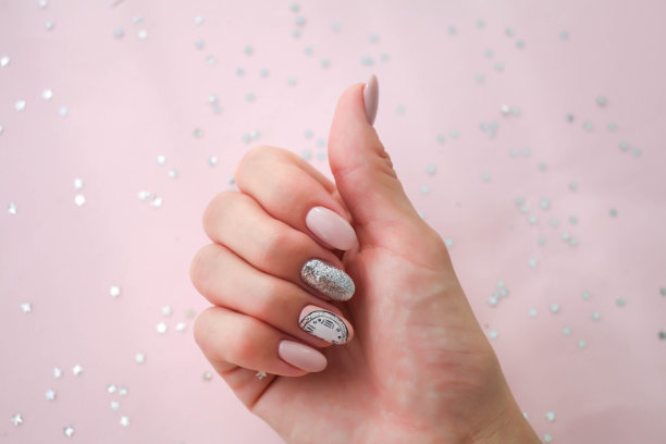 美丽的女性手与圣诞节钉子设计在粉红色的背景。指甲设计，指甲与时钟图案。亮片。虫胶,凝胶波兰。图片下载