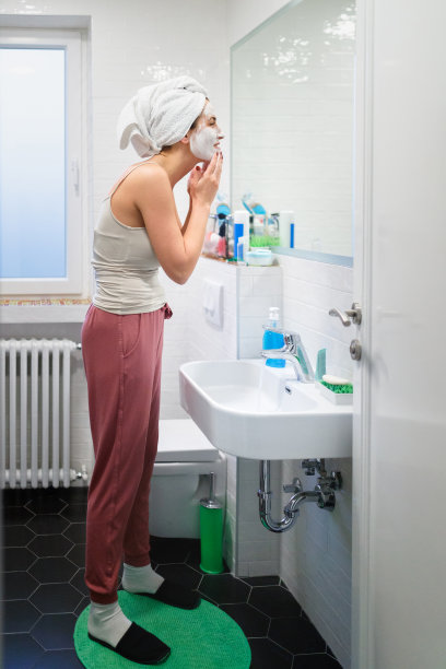 在浴室镜子前涂抹面霜的女人的侧影图片下载