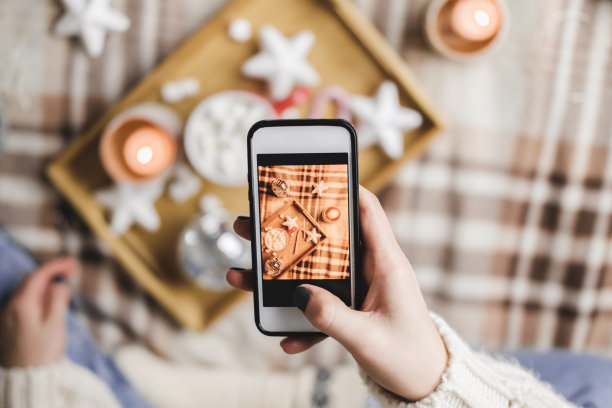 女性手用智能手机为社交网络拍摄新年或圣诞节的平面照片。为假期做准备，创造内容。木制托盘，可可杯，棉花糖，蜡烛，星星。图片下载