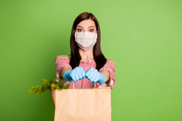 照片女孩送消费者顾客纸袋新鲜的杂货店市场草药自我隔离的概念戴医用口罩蓝色手套红色白色脱肩衬衫孤立的绿色背景图片下载