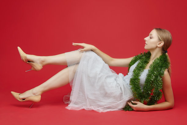 有魅力的女孩躺在红色的背景上，拿着圣诞装饰品图片下载