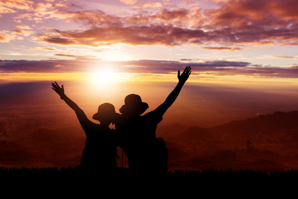 一对夫妇的剪影在山顶和天空日落的背景图片下载