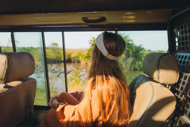 在坦桑尼亚，一名年轻的女游客在一辆汽车上看湖里的河马图片下载