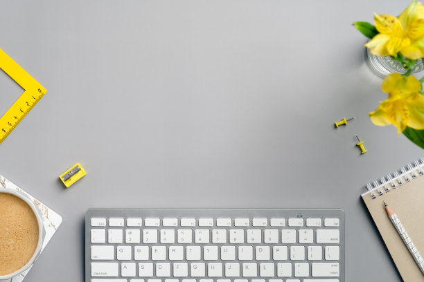 有电脑键盘，黄色文具，鲜花，咖啡杯和笔记本在灰色背景的家庭办公桌子。平铺，俯视图，拷贝空间。时尚色彩的自由职业者工作空间。图片下载