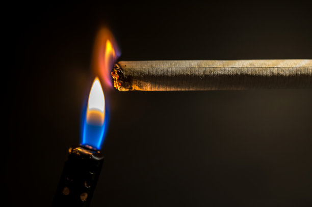 打火机的火焰在黑色背景下点燃一支香烟图片下载