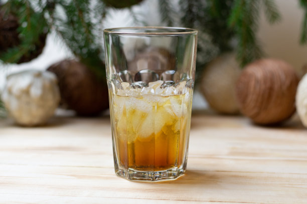 金色的朗姆酒，冰和可乐放在木桌上，圣诞树和球装饰图片下载