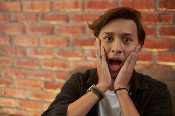 一个男人的肖像，嘴张得大大的，表情震惊地看着镜头，以砖墙为背景图片下载