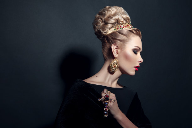 一个金发女孩的特写形象与美发，化妆，手持十字架，在黑色的背景。图片下载