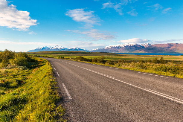在冰岛雪峰前的绿色草地上的柏油路图片下载