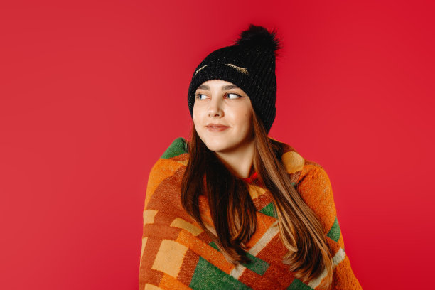 漂亮的女孩戴着冬天的帽子，裹着温暖的格纹，看着一边。图片下载