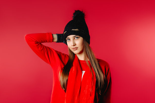 可爱的女孩摆姿势在红色的背景在冬天的帽子和手套。图片下载