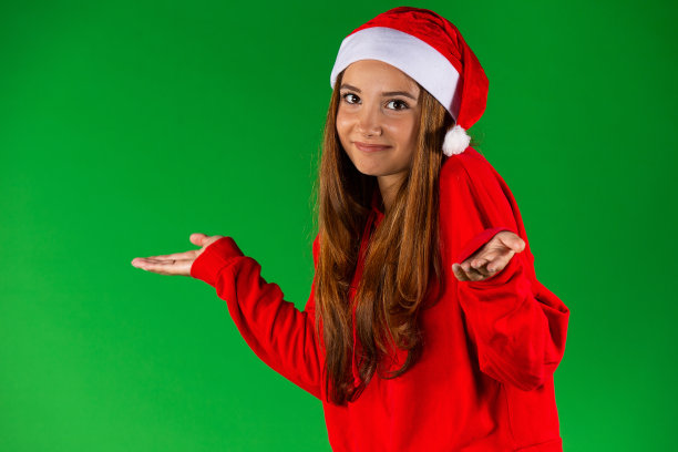美丽的白种女人在圣诞老人的帽子和红色套衫显示一些空的手，孤立在绿色的背景图片下载
