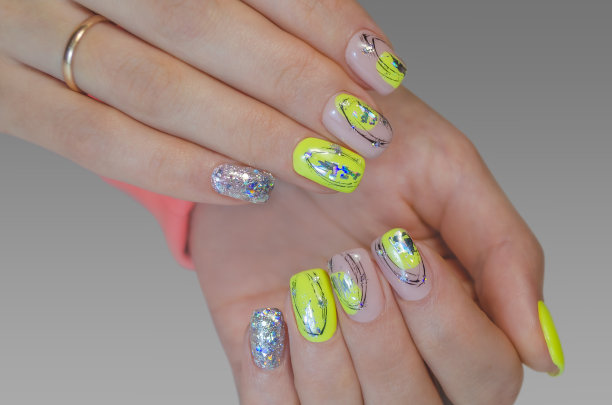 一个年轻女子的手，涂着黄色的指甲油，灰色的背景上有亮片。修指甲的想法。图片下载