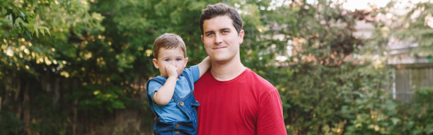 父亲的一天。快乐的白人父亲抱着一个小男孩在后院。父母和孩子在户外。真实的生活方式触动温柔的瞬间。网页横幅标题。图片下载