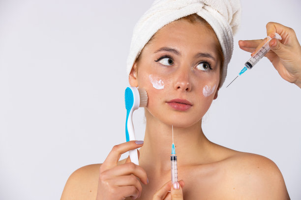 一个年轻女孩的肖像与毛巾在她的头上。这个女孩面临着一个选择，注射化妆品还是健康的皮肤护理。照片背景明亮图片下载