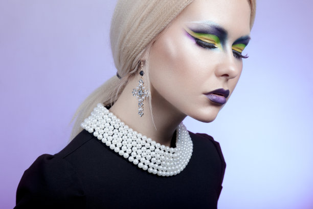 女模特金色头发，闭着眼睛化妆，戴着珍珠项链和十字耳环，紫色背景。图片下载