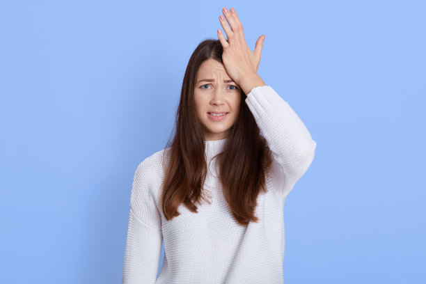 沮丧健忘的年轻女子带着焦虑的表情看着镜头，手心顶在头上，女性意识到她忘了一些重要的东西，在蓝色背景下摆出孤立的姿势。图片下载