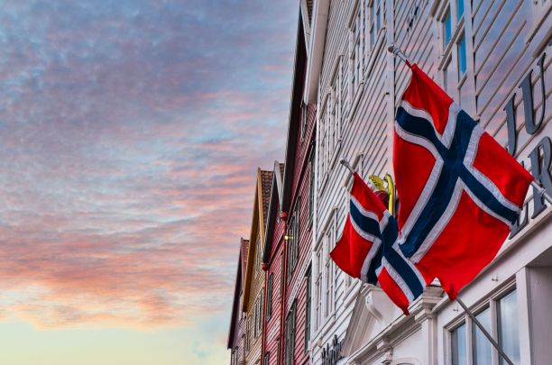 挪威国旗在美丽的日落天空下，在卑尔根一座老木屋的墙上随风飘扬。图片下载