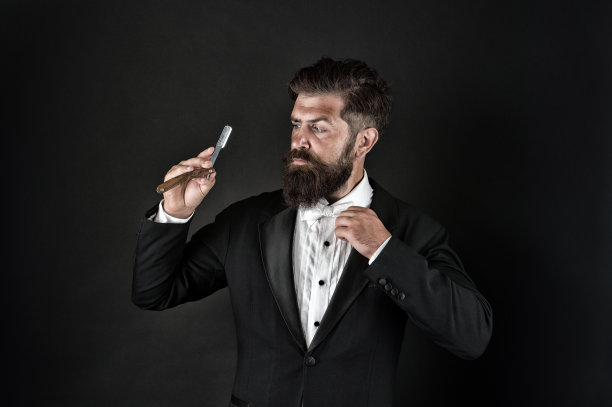 复古的吸引力。有胡子的男人拿着复古剃须刀。专业理发师深色背景。复古的理发店。理发店。专门从事经典剃须。美发沙龙。复古和古典，复古滤镜图片下载