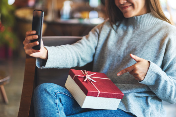 一个年轻漂亮的亚洲女人用手机和礼品盒自拍图片下载