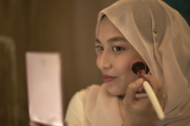 肖像微笑美丽的年轻穆斯林妇女戴着头巾，做面部化妆镜和化妆刷图片下载