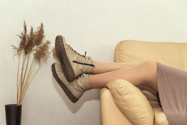 一个穿着靴子的女人坐在沙发上，旁边放着一瓶干花图片下载