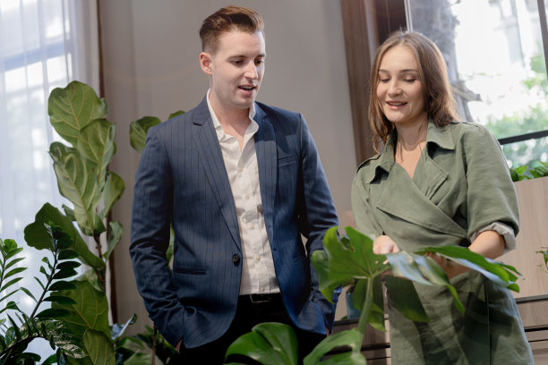 肖像快乐的商人和妇女检查和对待绿色的树木植物叶子在室内建筑花园。亲生命的自然概念办公空间。图片下载