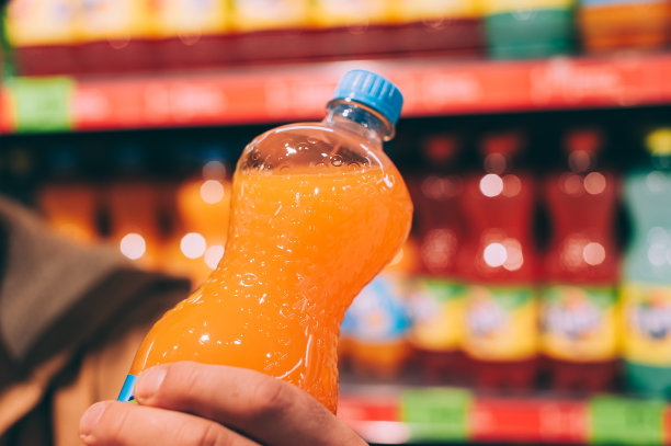 一个男人在超市里手里拿着一瓶甜饮料。图片下载