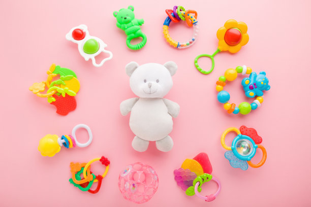 不同的彩色拨弄围绕白色的泰迪熊在浅粉色的桌子背景。柔和的颜色。特写镜头。给宝宝玩玩具。自顶向下的观点。图片下载