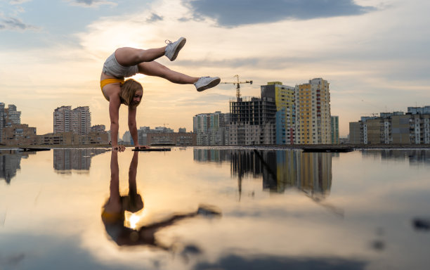 柔韧性的女子体操运动员做倒立和健美操与在城市景观背景的水在戏剧性的日落图片下载