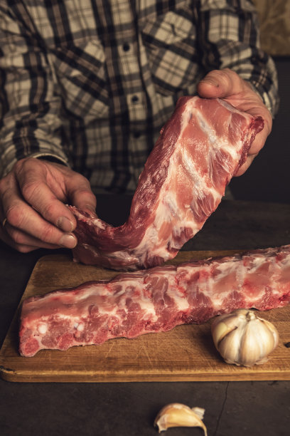 新鲜的排骨，烹饪与大蒜，多香木背景俯视图。男人的手握着肉图片下载
