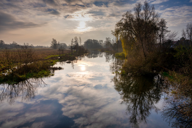 一条河中树和云的倒影的背光照片。美丽的日落天空在背景。图片来自瑞典斯卡尼亚县图片下载