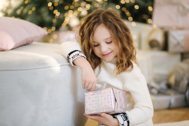 小女孩在圣诞树前打开礼物的肖像。背景的散景图片下载
