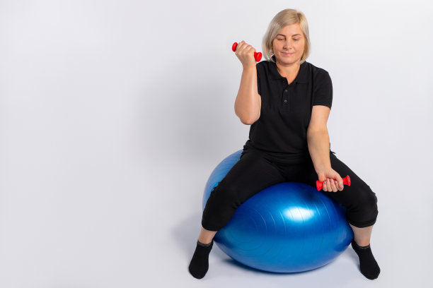 老年妇女在健身球上用哑铃做运动。白色背景。图片下载