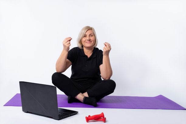 一位上了年纪的妇女盘腿坐在地板上的笔记本电脑前冥想。图片下载