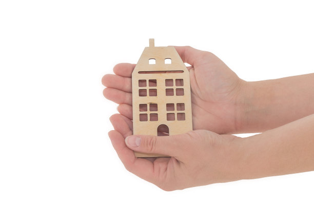 一个两层楼的房子模型躺在妇女的手掌上。照片上的白色背景，孤立，特写。这个概念是慈善，帮助，照顾那些需要帮助的人，照顾孤儿院的孩子。图片下载