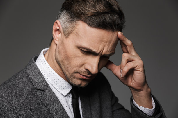 照片的特写英俊的成年男子30岁向下看，集中与触摸额头与手指，孤立的灰色背景图片下载