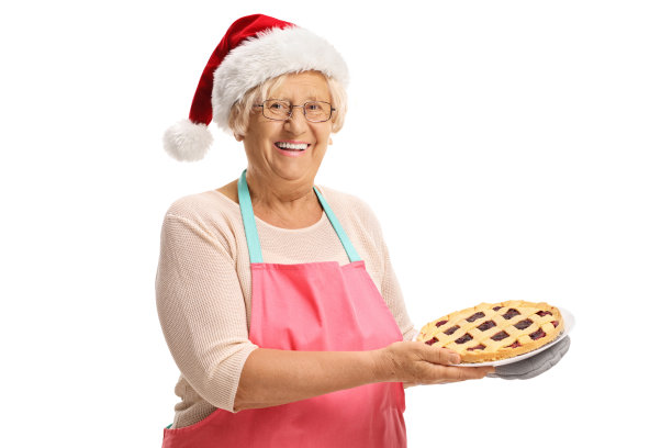 老妇人戴着圣诞老人帽，手里拿着刚烤好的圣诞派图片下载