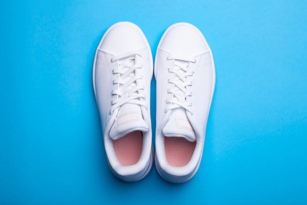 一双时尚的运动鞋在蓝色的背景。在彩色背景上的两个白色运动鞋俯视图图片下载