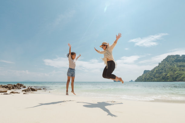 亚洲妇女母亲和女儿跳上空中，在海滩上玩耍，享受美丽的自然一起。图片下载