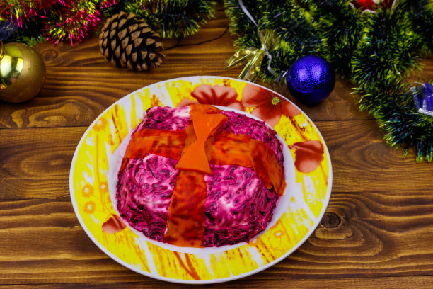 传统的俄罗斯沙拉“皮草下的鲱鱼”(舒巴)和木制桌子上的圣诞装饰品。做成礼品盒形状的沙拉图片下载