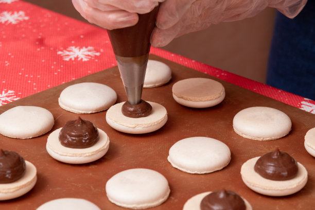 糕点师把馅料放在一半的蛋白杏仁饼干上。制作圣诞甜点的过程。有选择性的重点。图片下载