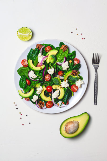 沙拉配以菠菜、羊乳酪、圣女果、花椰菜、鳄梨和核桃，配以青柠汁，以白色为背景——这是减肥食品的概念。垂直平铺，为你的文本复制空间图片下载
