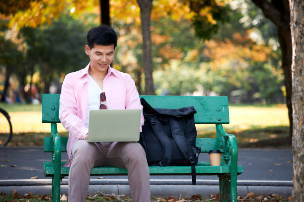 一个亚洲人在公园里用笔记本电脑工作。图片下载
