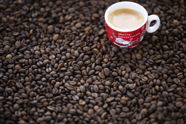 一个圣诞杯和一些奶油咖啡放在一些烤咖啡豆上。图片下载