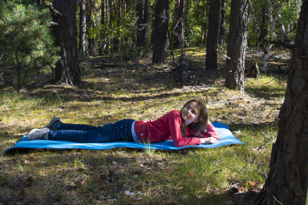 一个长头发的女孩躺在树林里的蓝色垫子上图片下载