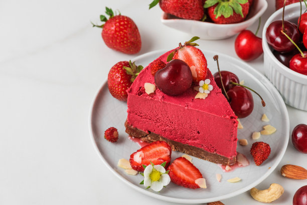 一片生的纯素浆果芝士蛋糕无麸质和乳制品与新鲜浆果，坚果和鲜花。素食餐后甜点素材图片