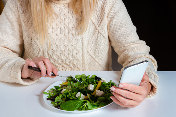 中年金发女人一边用智能手机一边在厨房吃沙拉，这是生活方式的概念图片下载